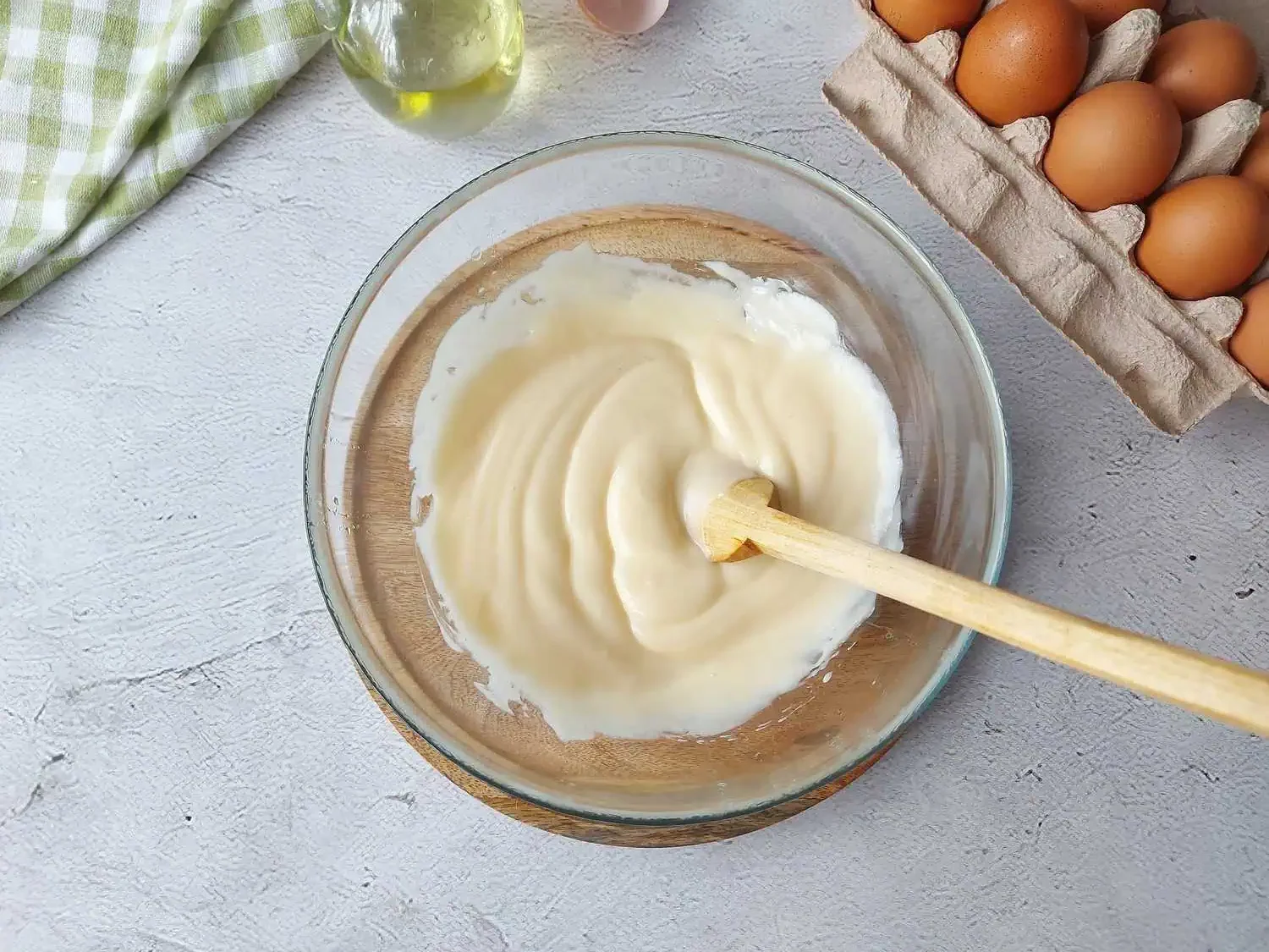 Homemade mayonnaise in a glass bowl with a wooden spoon