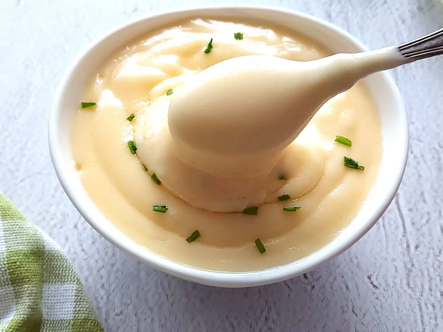 Small bowl with homemade mayonnaise recipe, with a sprinkle of chives and spoon 