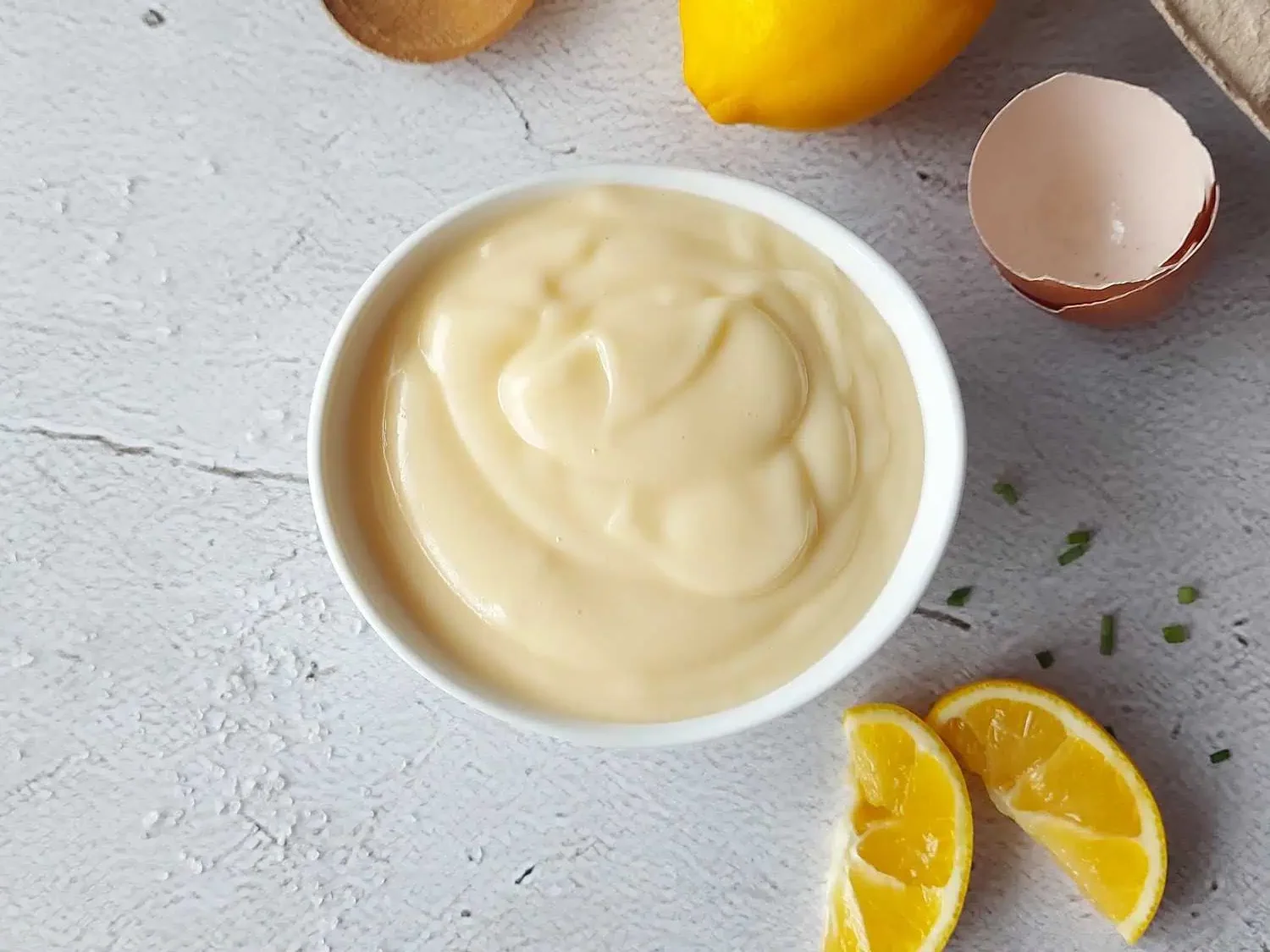 Classic Mayonnaise next to lemon, egg shells and a wooden spoon