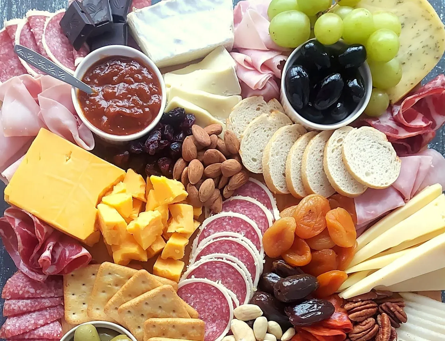 close-up of a charcuterie board with salami, cheese, crackers, dried apricots, dates. almonds, dried cranberries, olives and jams