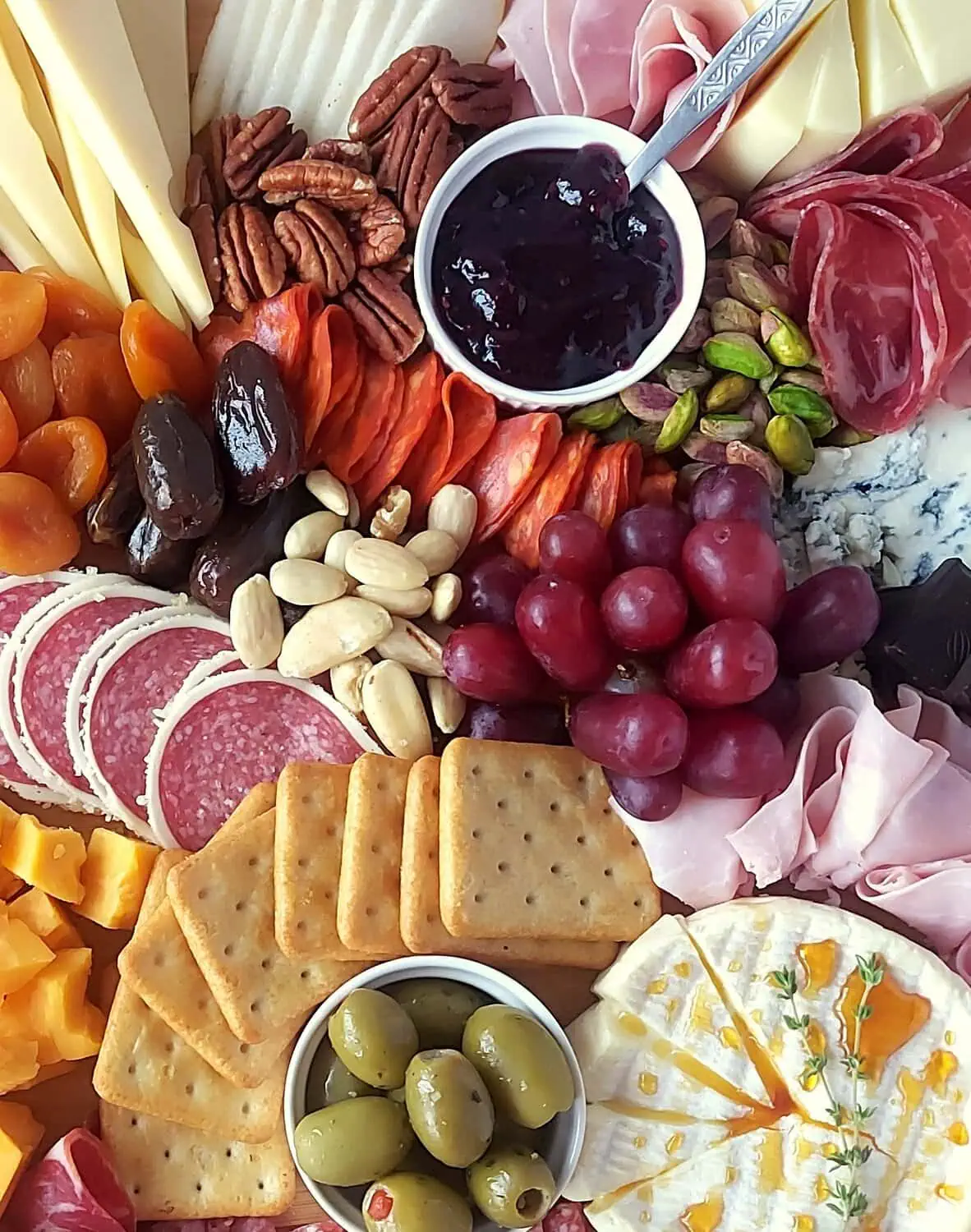 close-up of a charcuterie board with red grapes, cheese, meat, crackers, jam, dried apricots, dates, pistachios, pecan nuts, olives and blue cheese