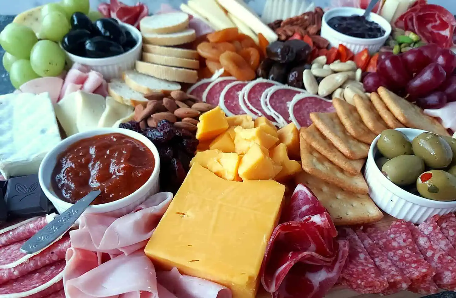 side image of a cheddar cheese, salami, jams, nuts, and crackers