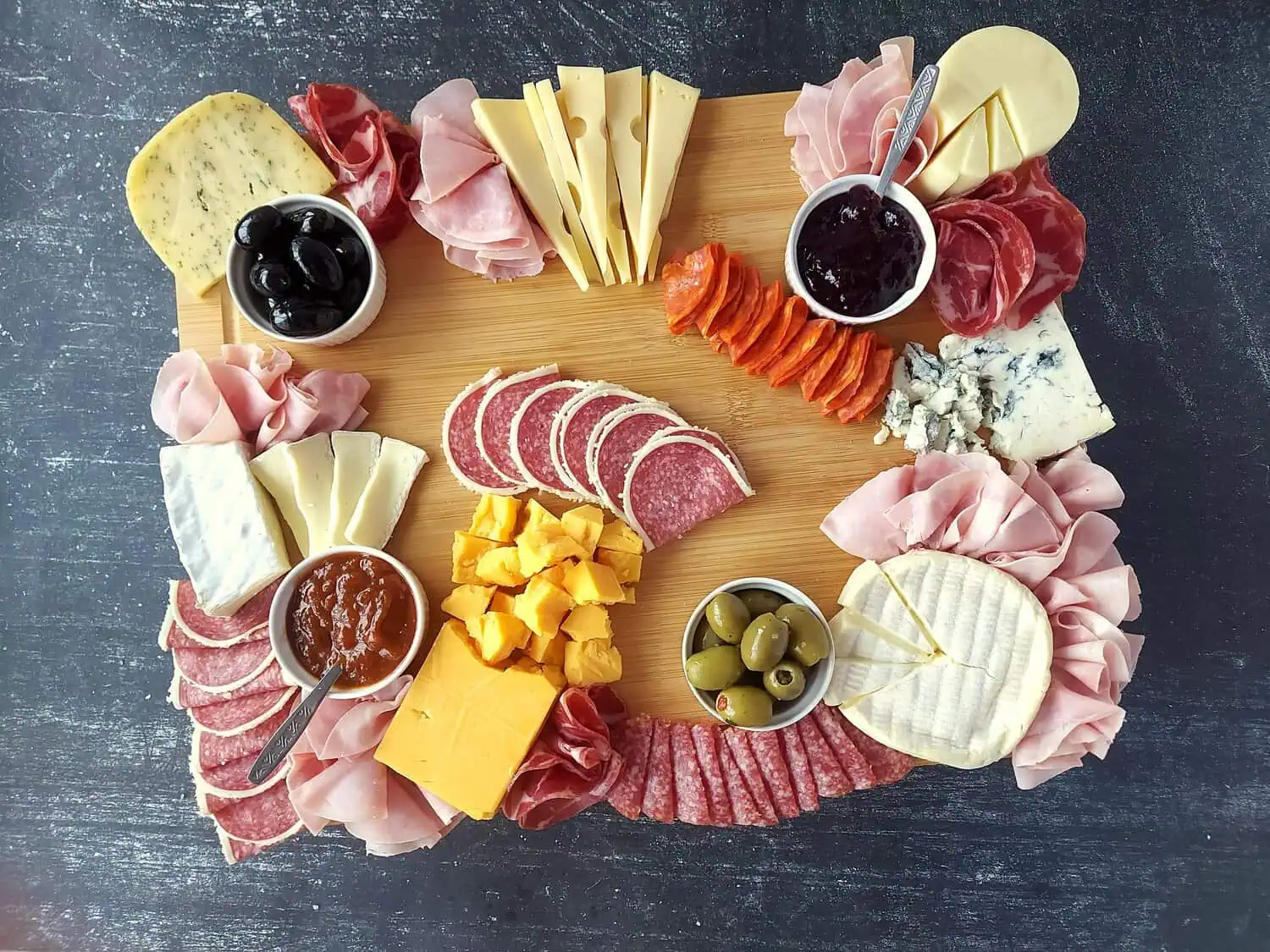wooden board with cheese, meats, olives and jams