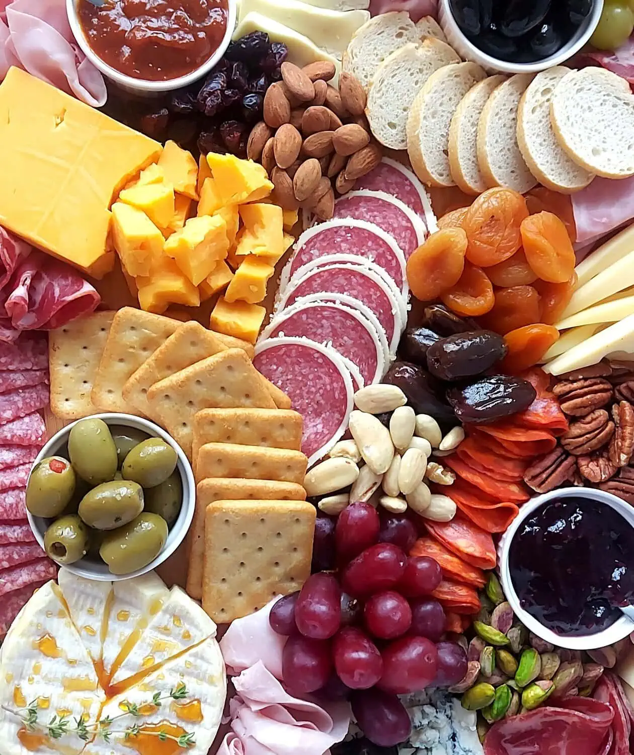 close up of a charcuterie board with cheese wedges, chorizo, red grapes, Marcona almonds, pistachios, blues cheese, crackers, dried apricots, and pecan nuts