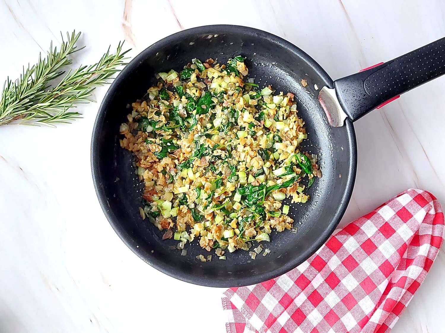 cranberry apple stuffed pork loin Sautéd onions, celery, garlic, bacon and spinach in a pan next to a red and white napkin