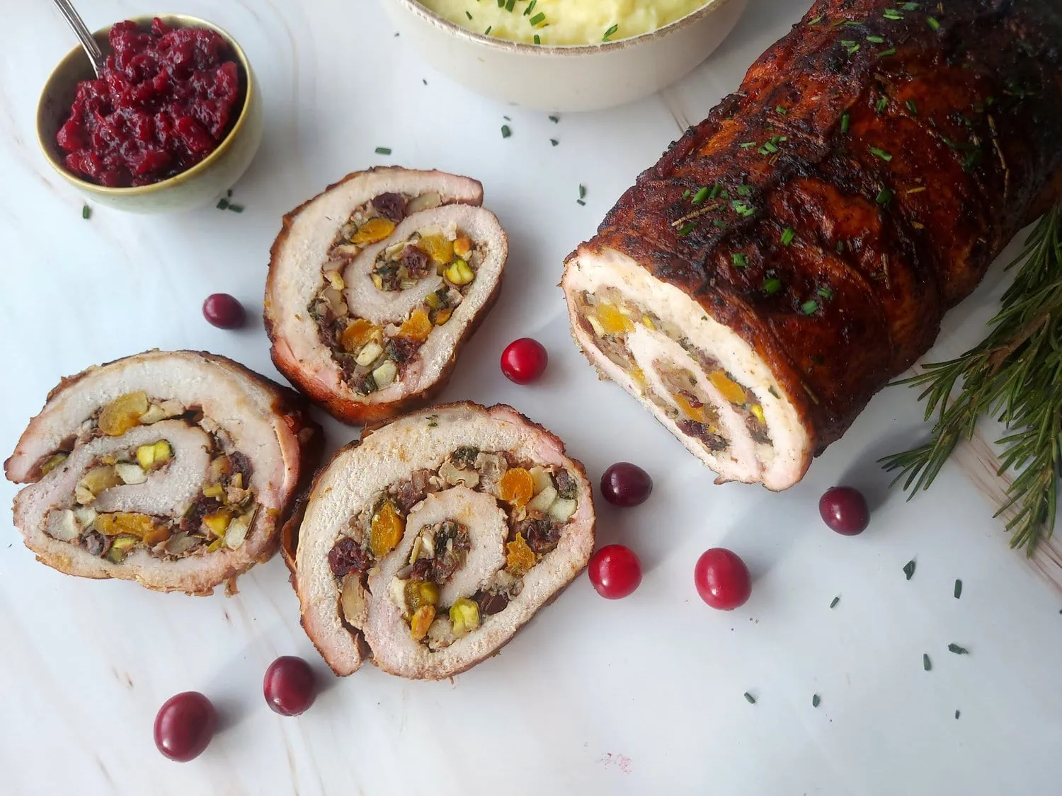 cranberry apple stuffed pork loin Overhead shot of an apple stuffed pork loin with cider sauce, next to 3 slices of this roll and cranberry sauce