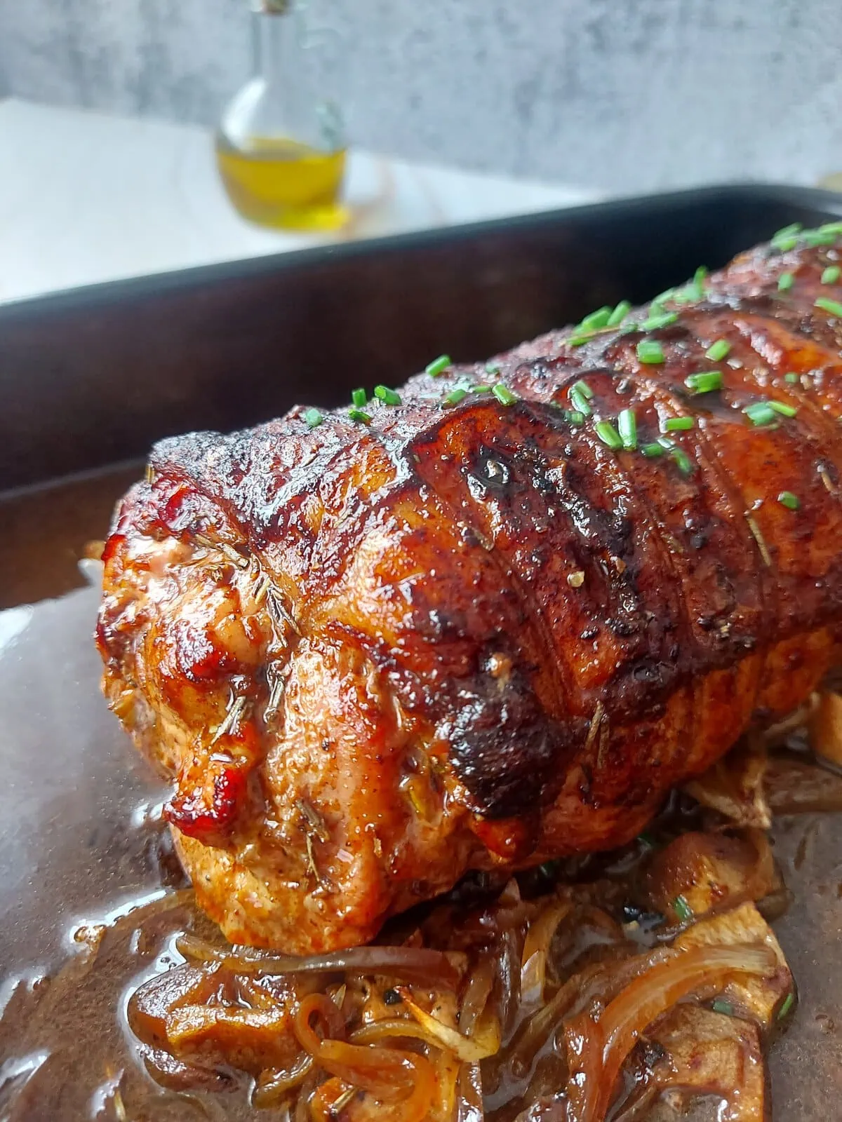 cranberry apple stuffed pork loin Close up shot of a nicely browned apple stuffed pork roast in a pan over a bed of apples and onions, with a sprinkle of chopped chives on top