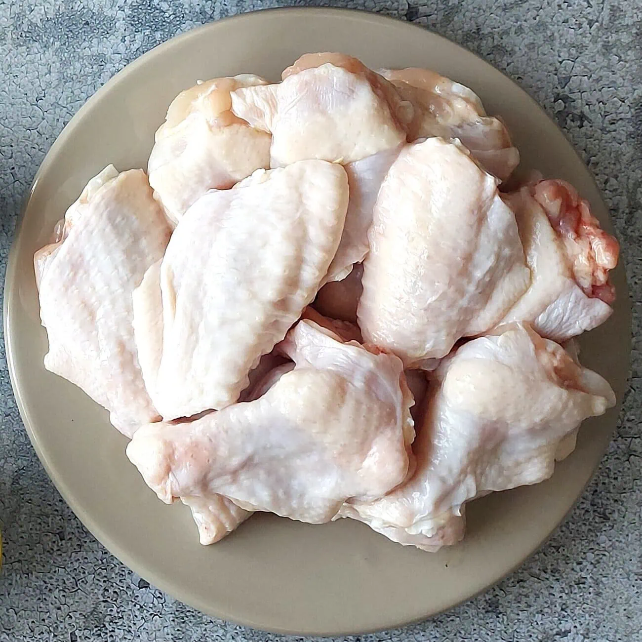 Raw chicken wings separated into drumettes and flats, on a beige plate