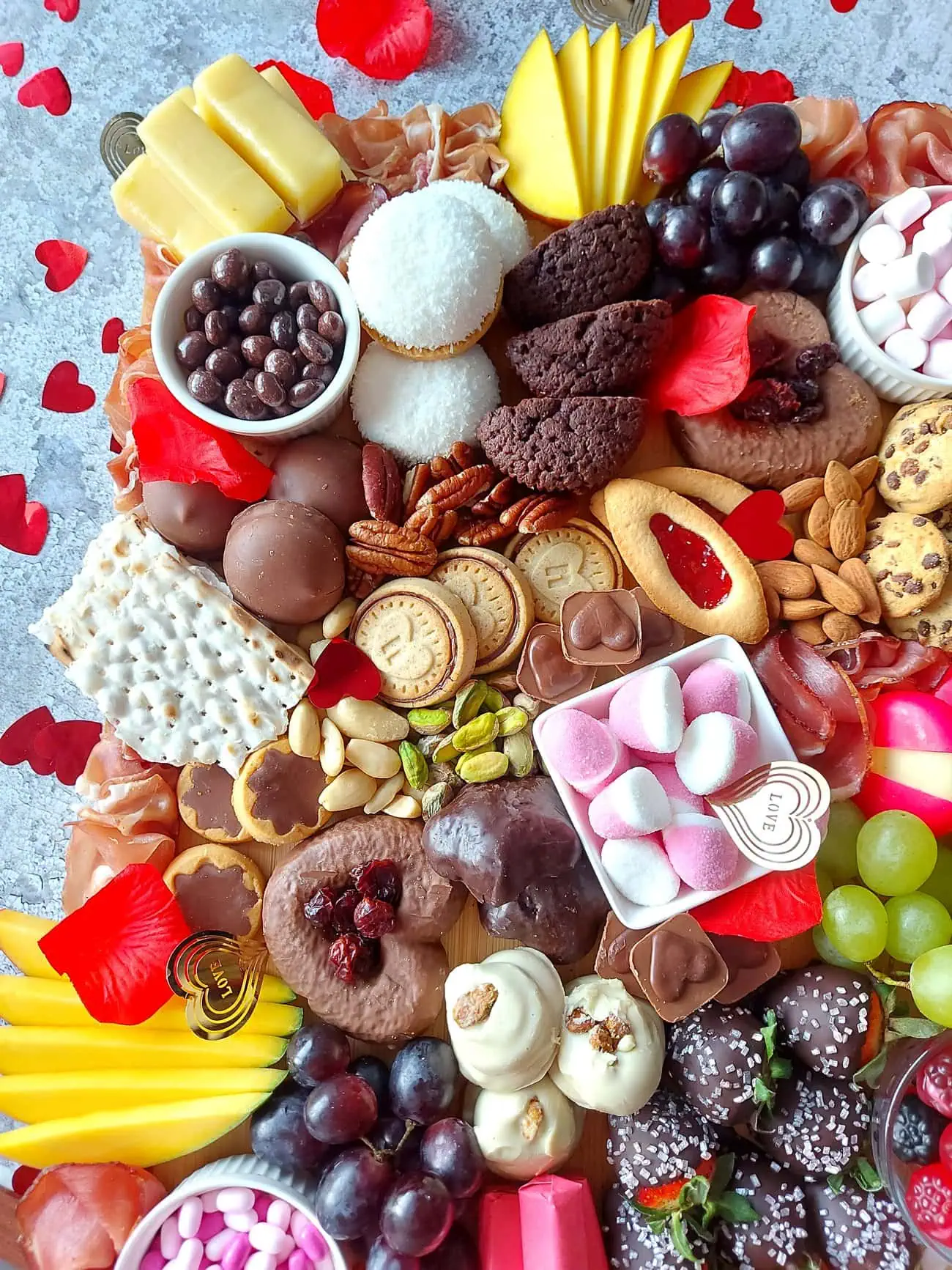 valentine's day charcuterie Overhead shot of a styled Valentine's charcuterie board with rose petals and confetti hearts around
