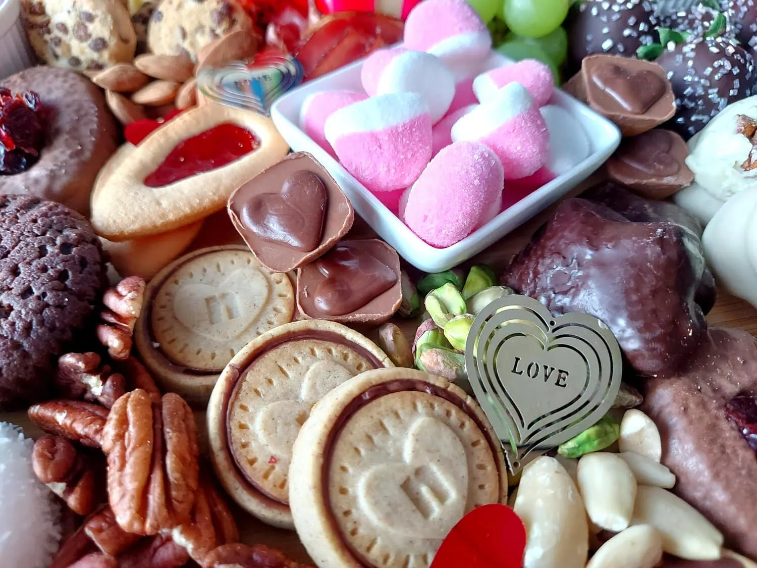 valentine's day charcuterie Close up of heart shaped chocolate biscuits, pink and white marshmallows, heart-shaped chocolates, Pecan nuts and almonds on a romantic grazing tray
