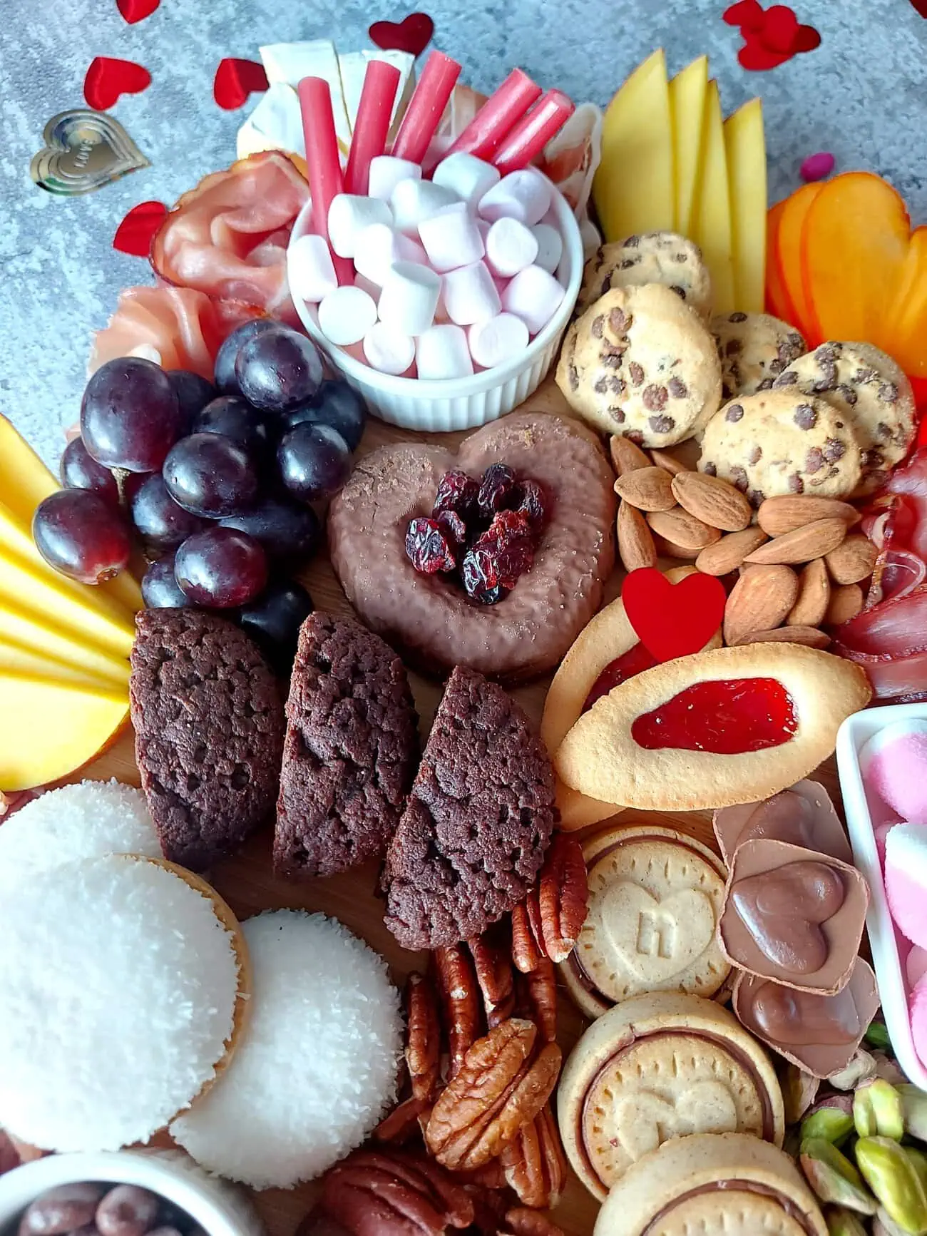 valentine's day charcuterie Close up of a romantic grazing board, with heart-shaped ginger bread, heart shaped chocolate biscuits, marshmallows, Pecan nuts, pistachios and chocolate chip cookies