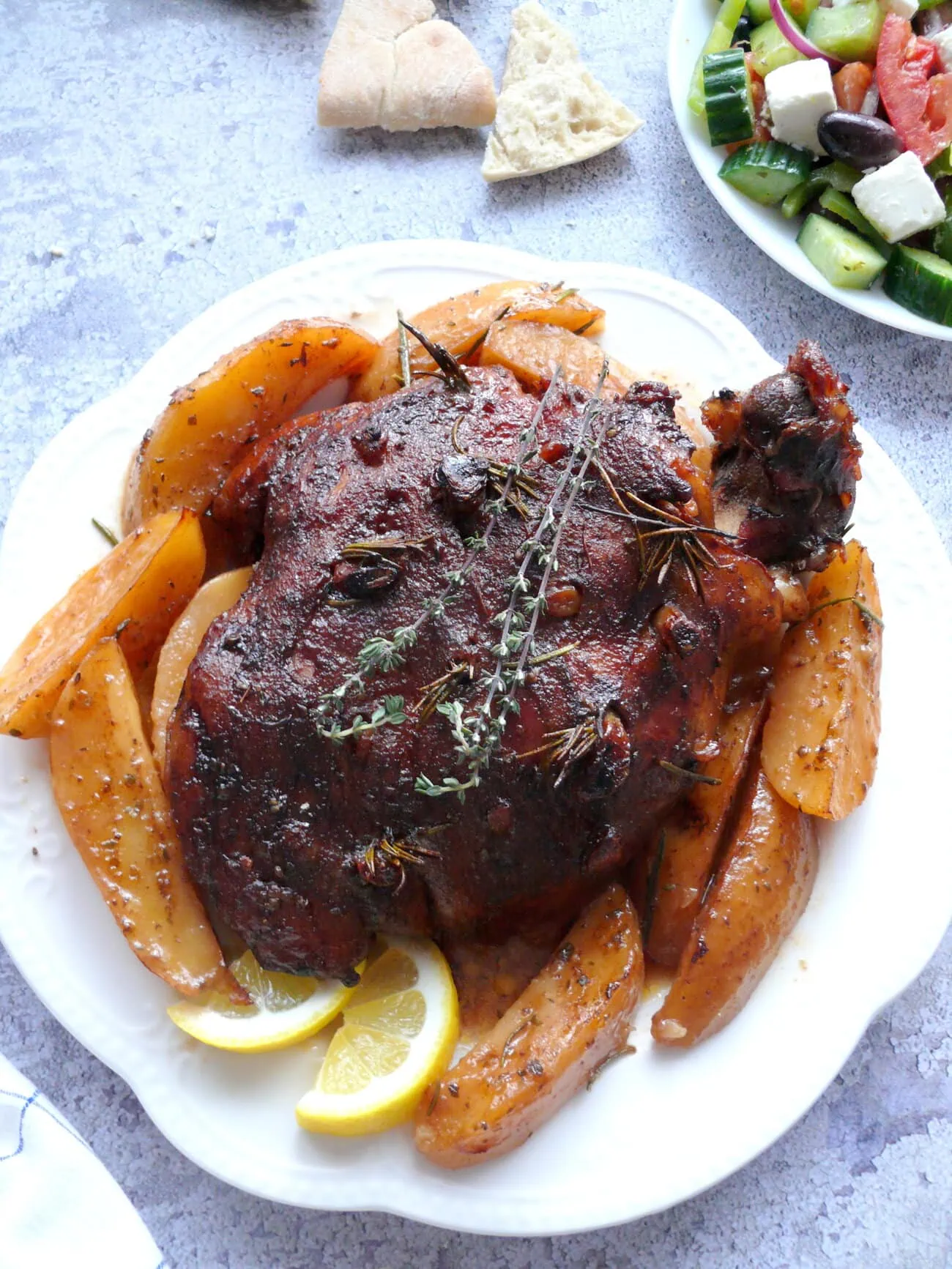 whole Greek style leg of lamb on a plate on a bed of greek lemon potatoes and lemon slices
