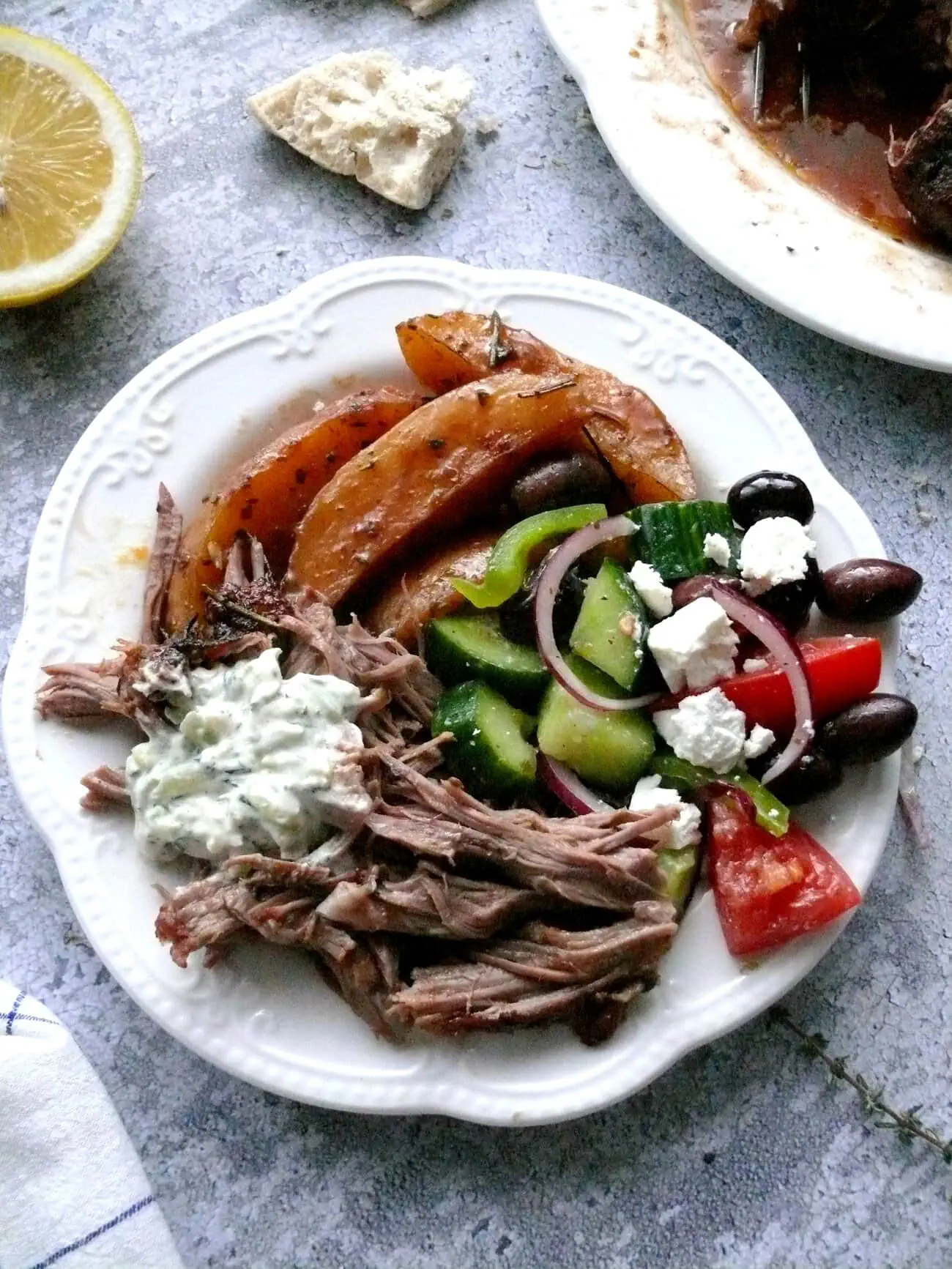 OVERHEAD SHOT OF A PLATE WITH SHREDDED LAMB MEAT, GREEK LEMON POTATOES, GREEK SALAD AND TZATZIKI SAUCE