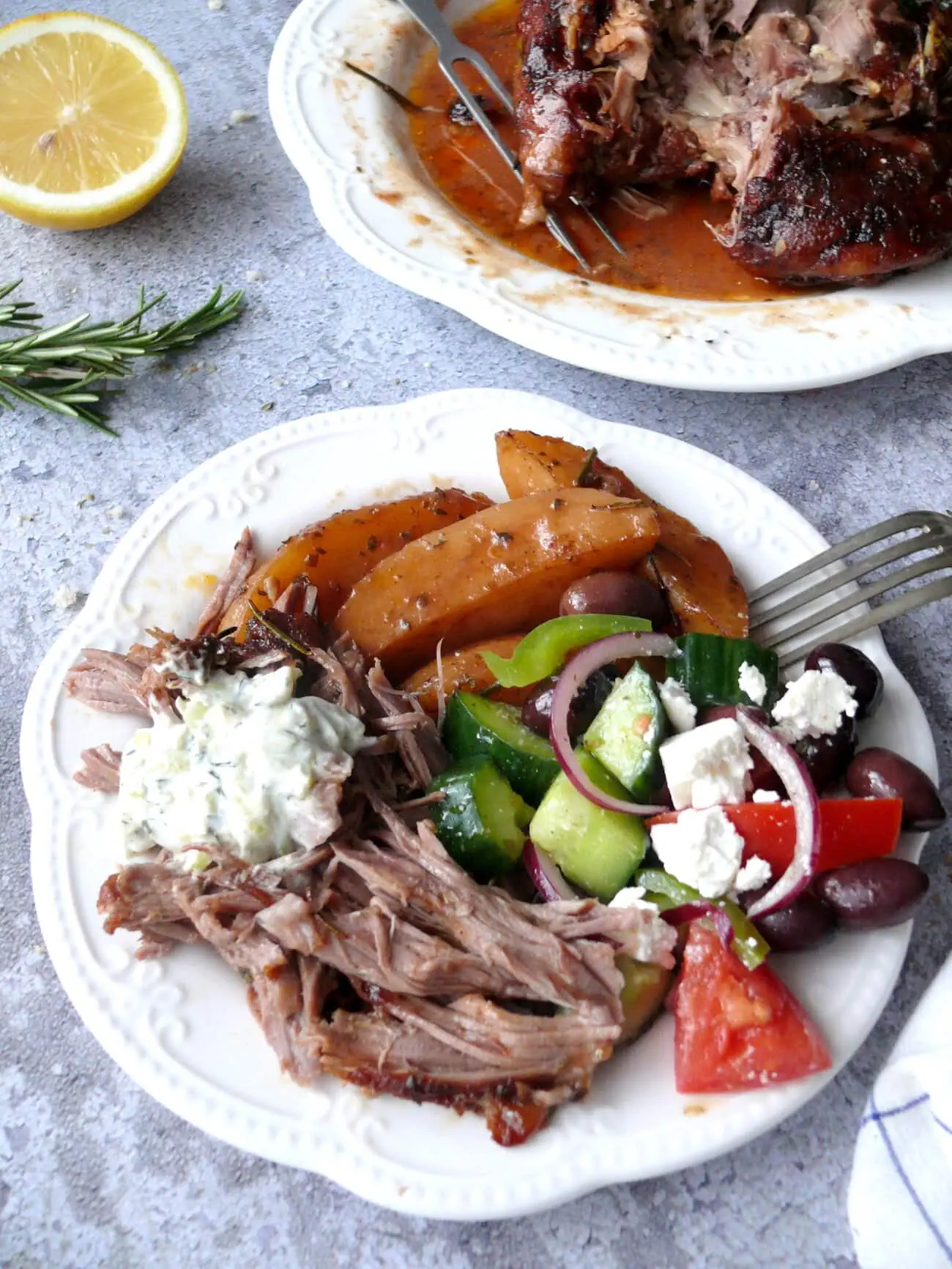 Plate with shredded lamb greek salad, oven roasted potatoes and homemade tzatziki dip