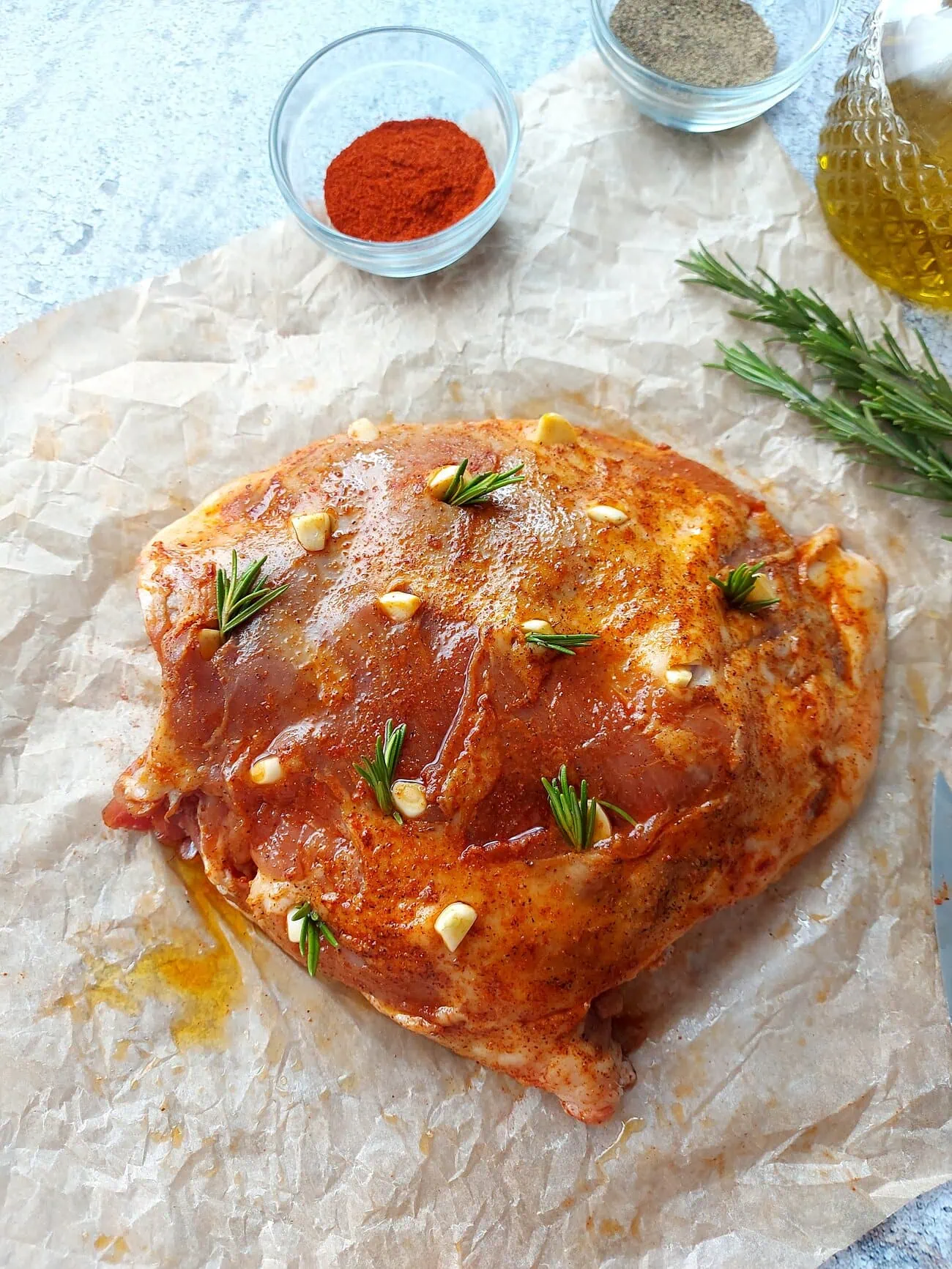 Raw leg of lamb rubbed with salt, pepper, paprika and stuffed with garlic cloves and rosemary sprigs