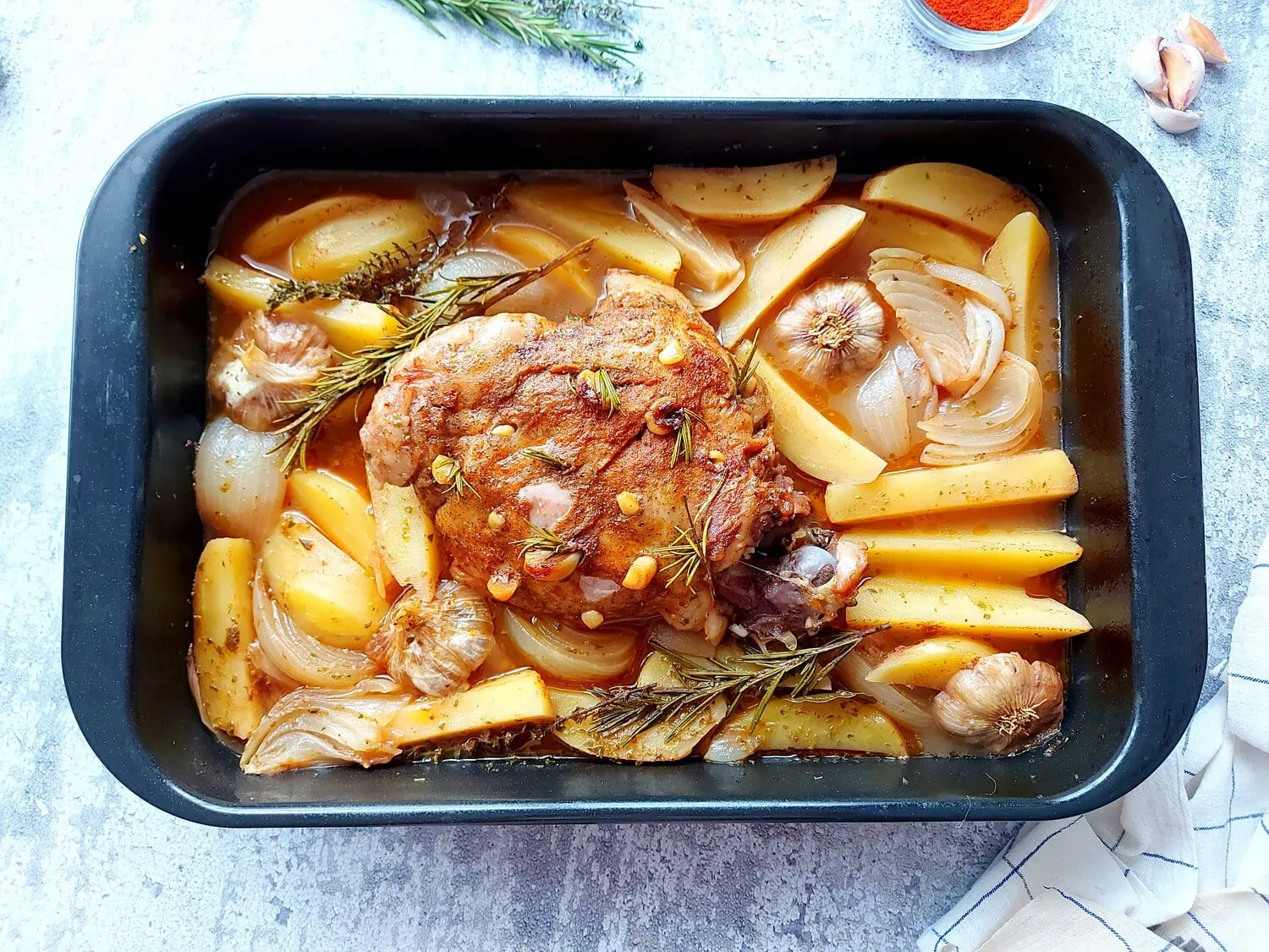 Cooked lamb in a roasting pan over potatoes and braising liquid
