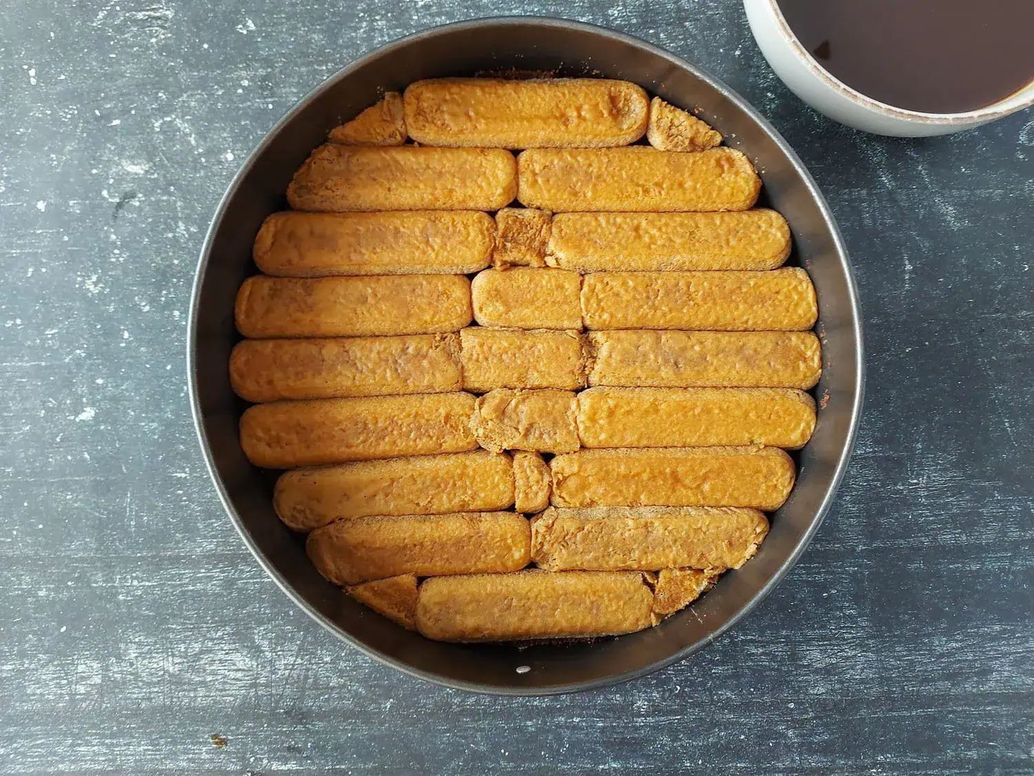 Bottom layer of coffee-soaked ladyfingers in a round pan