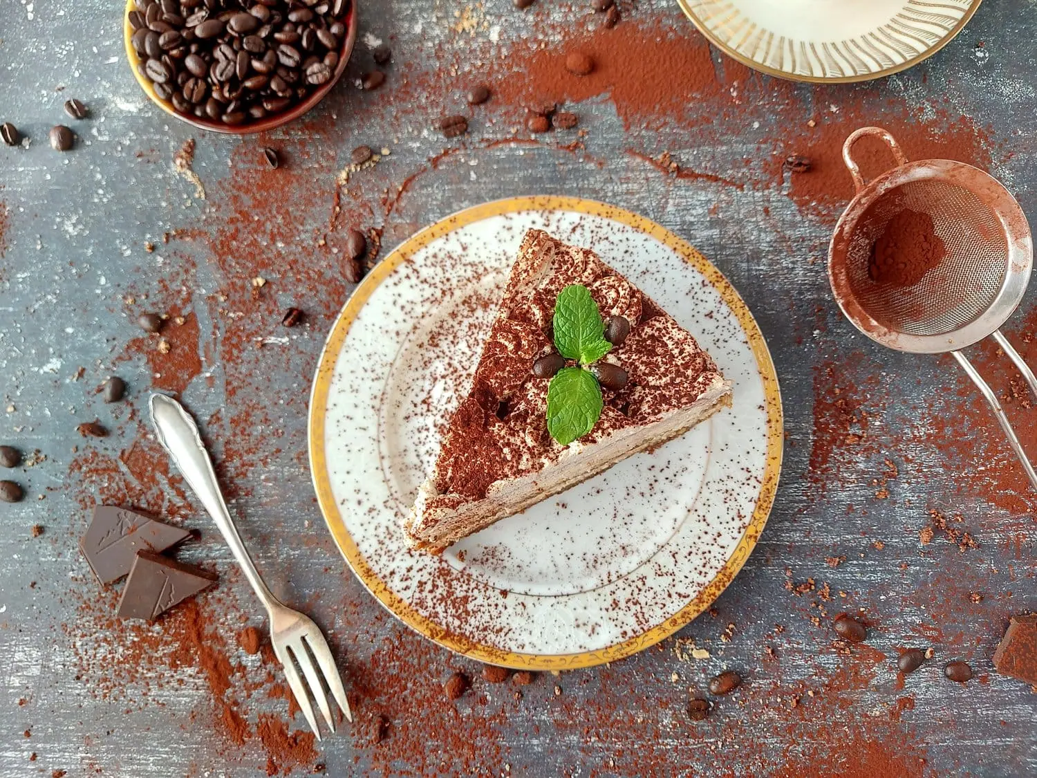 Overhead shot of a slice of no bake tiramisu cheesecake on a white plate with cocoa powder and coffee beans around 