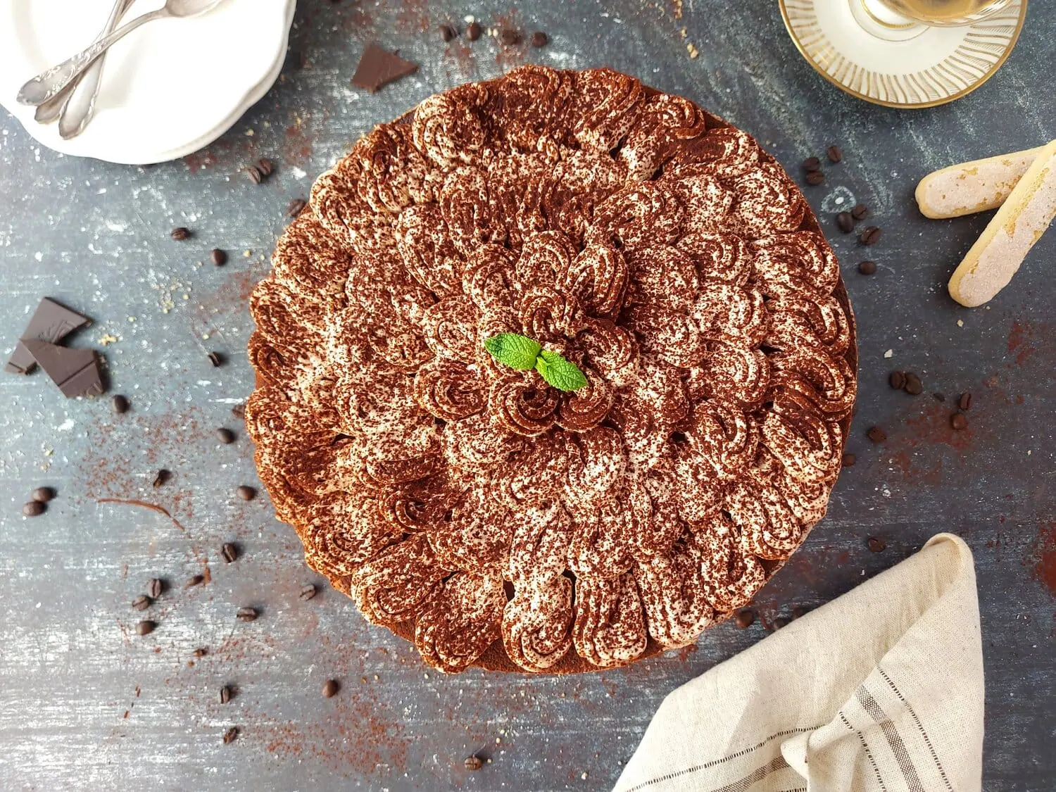 Overhead shot of a round no bake tiramisu cheesecake, a beige napkin, ladyfingers and some coffee beans