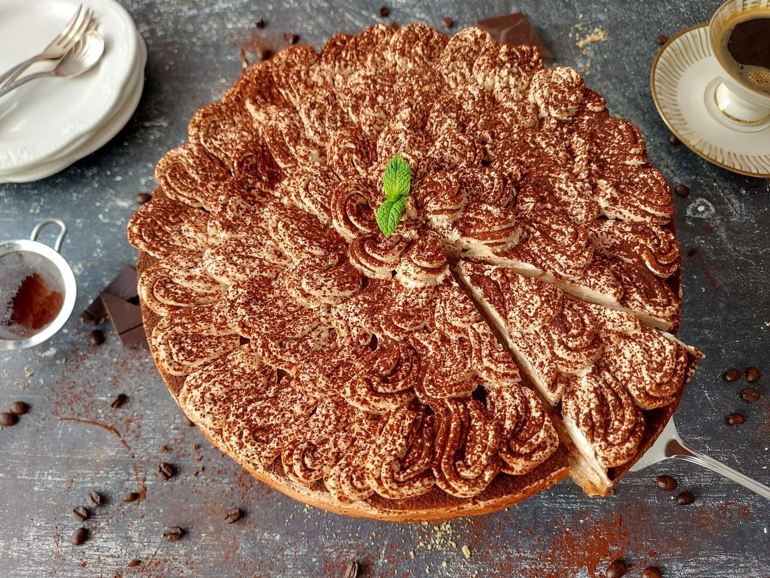 TIRAMISU CHEESECAKE WITH A SLICE BEING CUT OUT, COFEE BEANS AND DUSTED COCOA POWDER