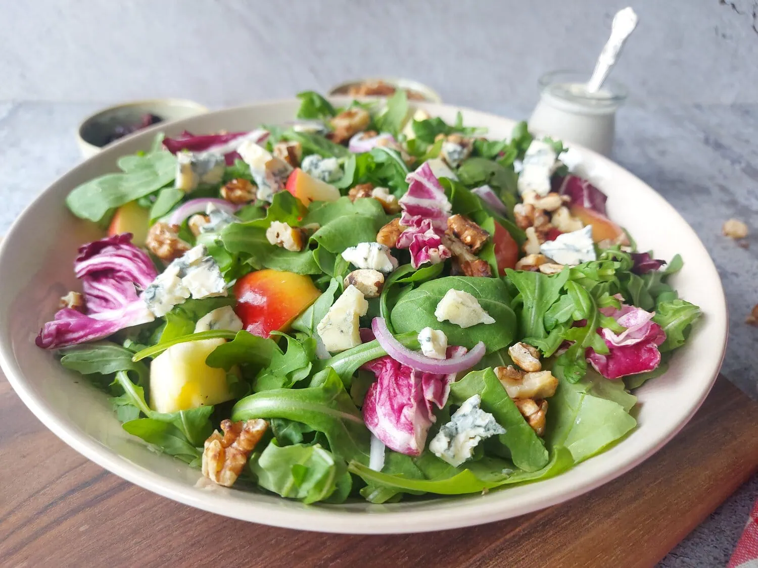 Salad greens on a plate with toasted walnuts, apple slices, red onion and cranberries