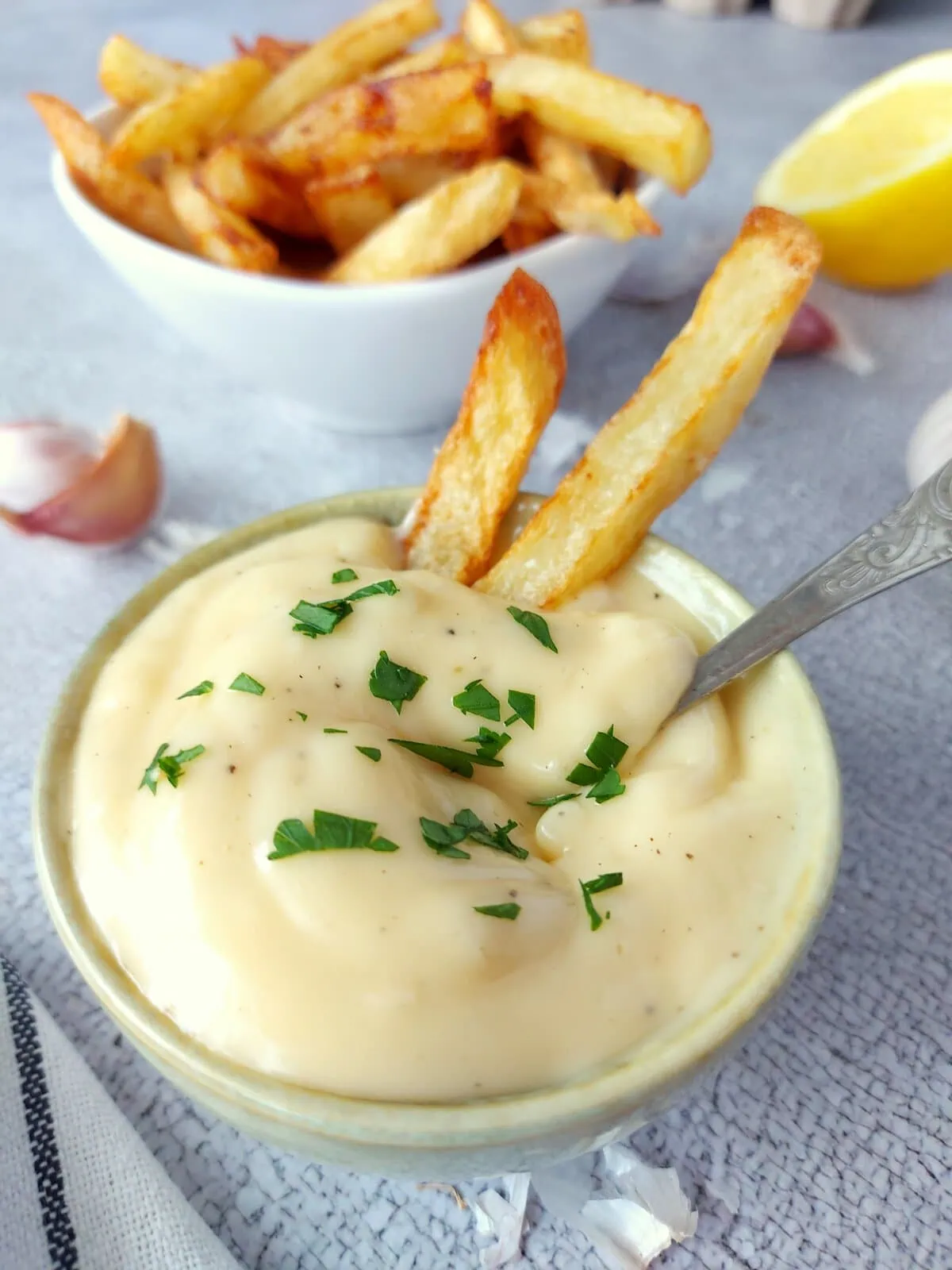 Garlic aioli sauce in a ramekin with French fries and a spoon