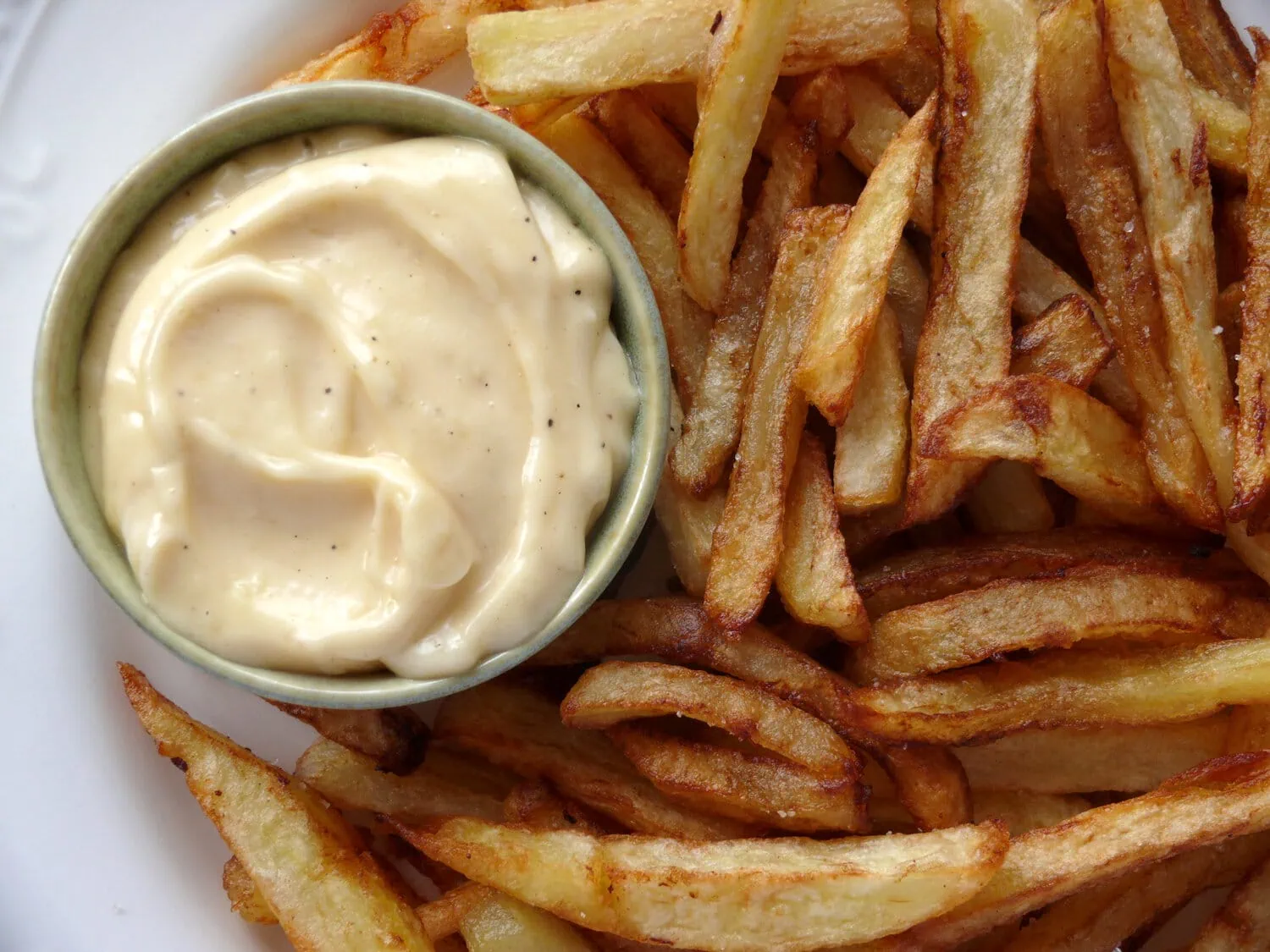 Homemade garlic aioli in a small bowl on a plate with French fries