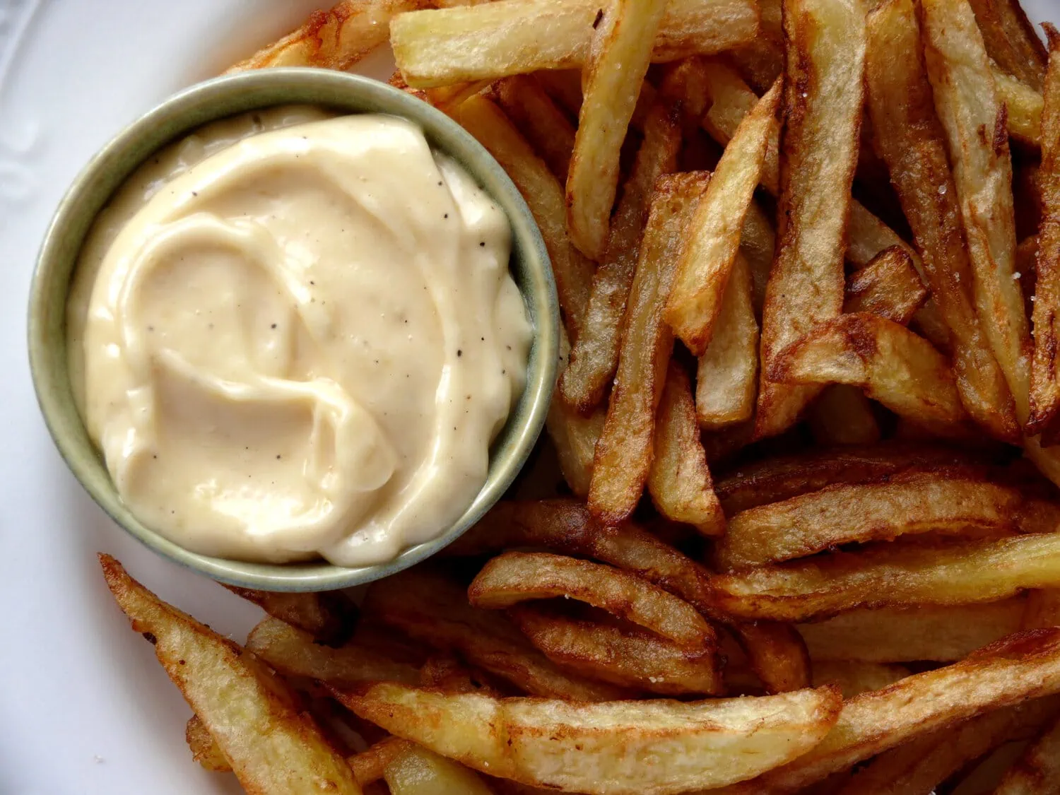 Ramekin with homemade garlic aioli on a plate with French fries