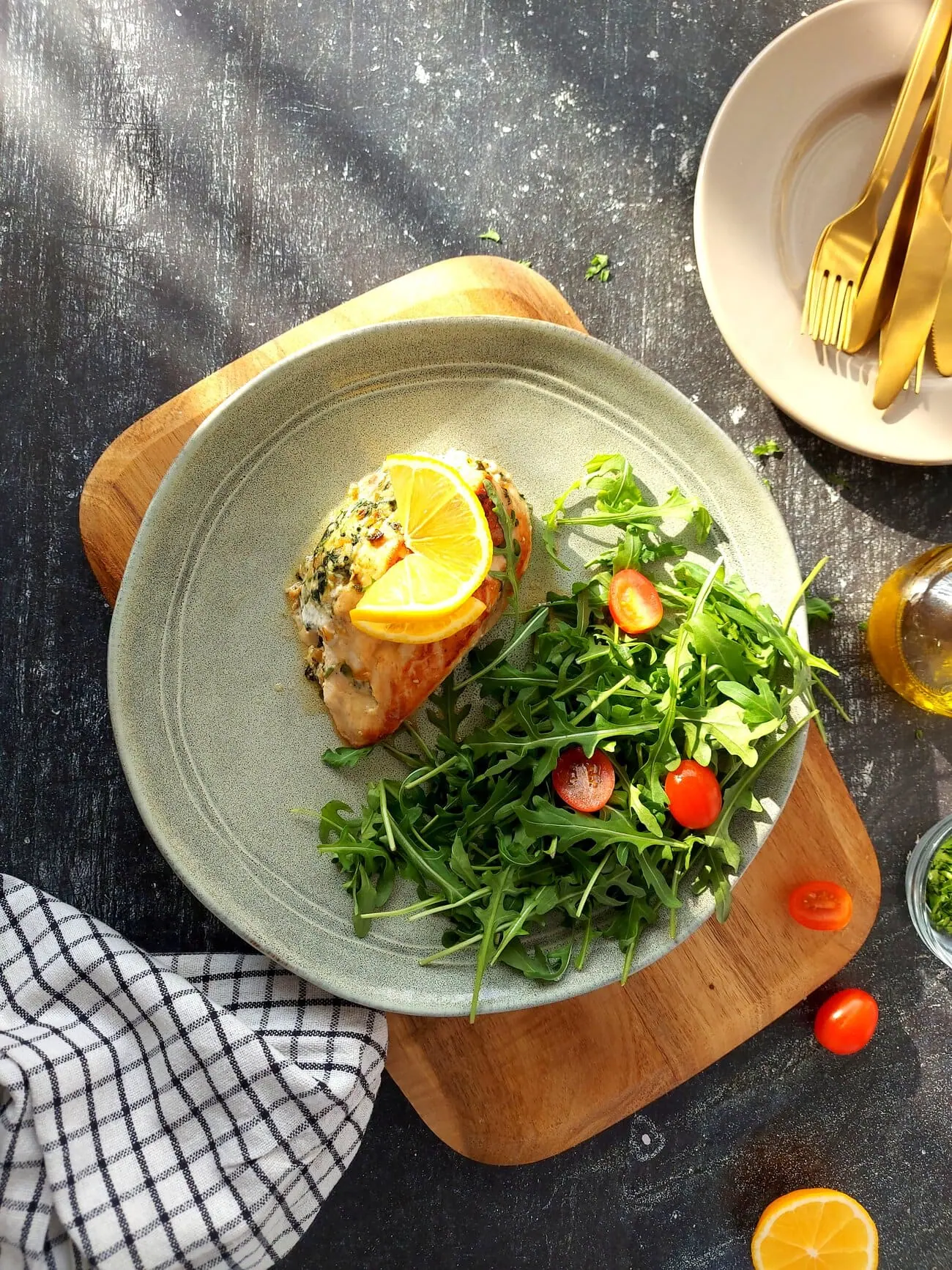 overhead shot of a ricotta stuffed chicken breast with a lemon slice on top served with arugula salad and cherry tomatoes
