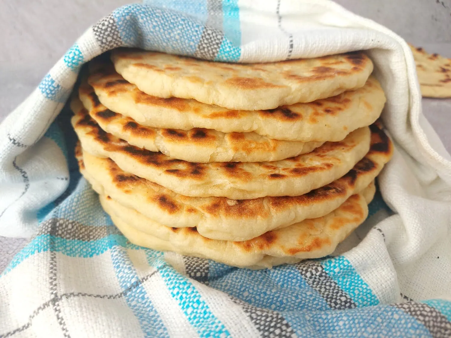 Fresh Greek pita bread cooling under a kitchen towel